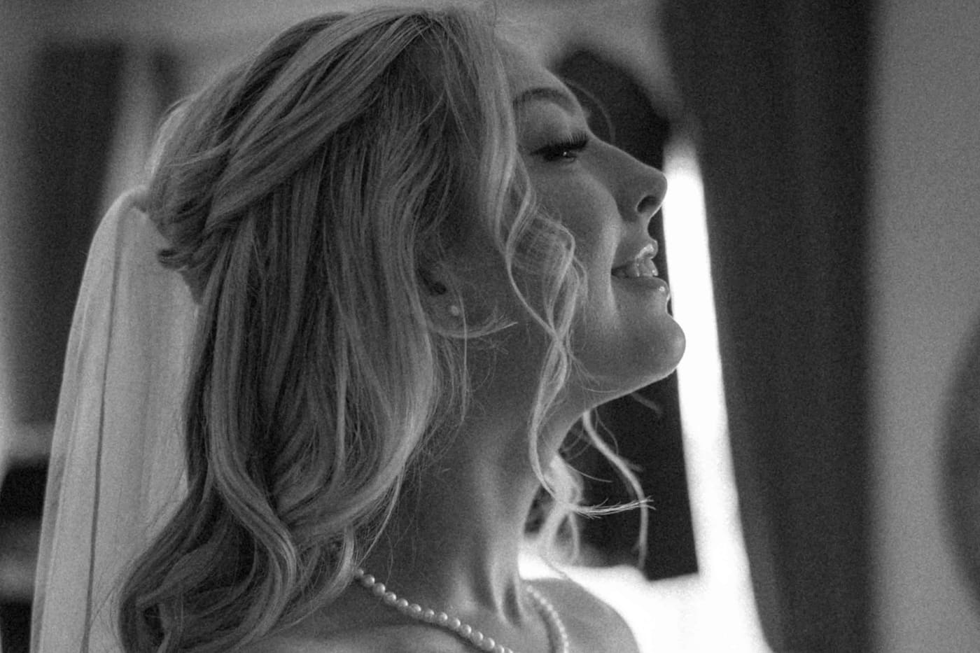 Mariée souriante avec une coiffure semi-attachée ondulée et un voile